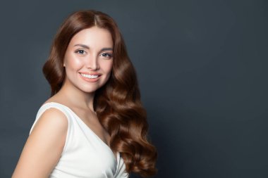 Gri arka planda gülümseyen güzel kadın. Kıvırcık saçlı güzel bir manken.