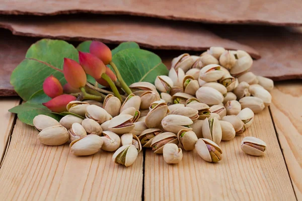 Tasty pistachio nuts with green leaves on wooden table background — Stock Photo, Image