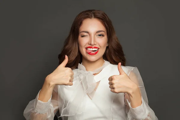 Hermosa mujer divertida guiñando un ojo, mostrando el pulgar hacia arriba y la lengua —  Fotos de Stock