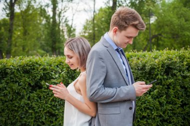 Genç bir kadın ve erkek açık havada akıllı telefon kullanıyor.