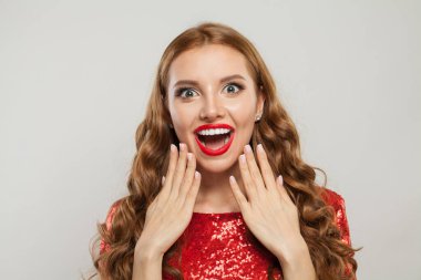 Uzun dalgalı saçları, kırmızı dudakları ve beyaz arka planda manikürlü tırnakları olan mutlu, şaşırmış bir kadın.