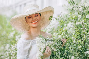 Açık havada beyaz şapkalı, çiçekli mutlu kadın portresi.