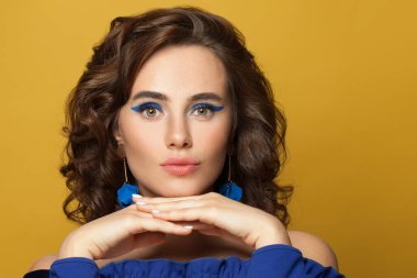 Parlak sarı arka planda kıvırcık saç kesimi olan güzel bir genç kadının moda portresi.