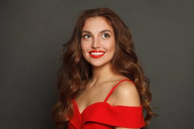 Siyah arka planda uzun saçlı ve makyajlı, gülen bir kadın. Kıvırcık saçlı, güzel bir kadın.