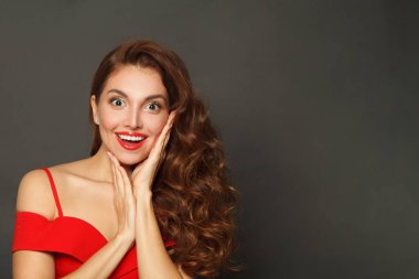 Joyful surprised woman with curly hairstyle and makeup holding her hand with her face on black background