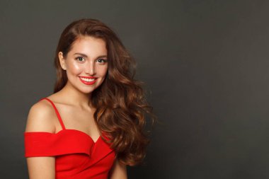 Glorious brunette woman with trendy make-up and brown curly hair wavy hairstyle and red lips makeup on black background 