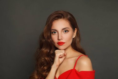 Calm brunette woman with trendy make-up and brown curly hair wavy hairstyle and red lips makeup on black background 