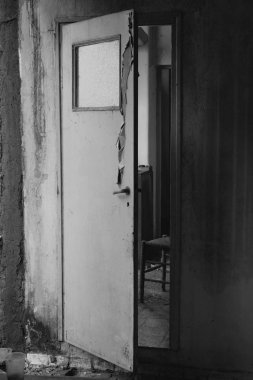Yarı mutfaktan eski terk edilmiş evde iç koridorda önde gelen gıcırdayan kapı açık. Siyah ve beyaz.