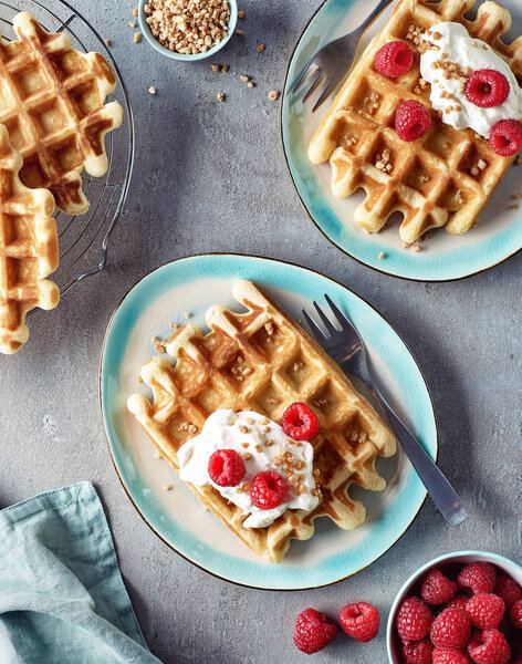 Two plates of belgian waffles with whipped cream and raspberries on gray marble background. Top view