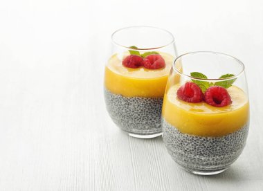 Sağlıklı vegan chia pudingle mango sos ve taze ahududu Beyaz ahşap zemin üzerinde
