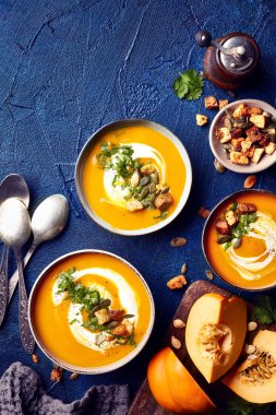 Balkabağı çorbası krem, tohum ve kişniş ile mavi arka plan üzerinde bırakır. Üstten görünüm