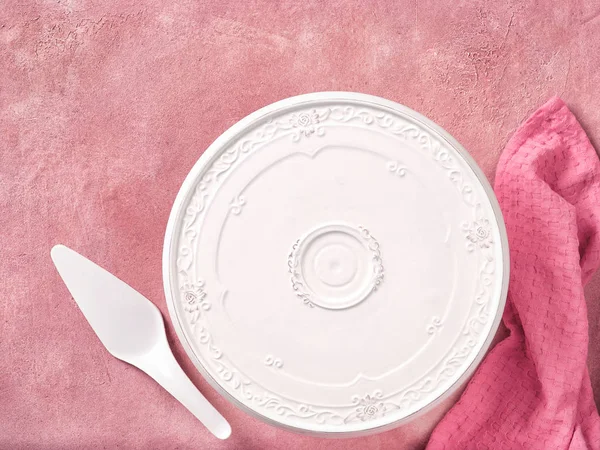 Empty cake plate and spatula on pink concrete background