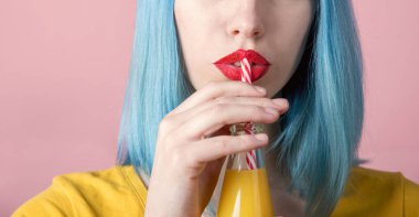 Portre stüdyo kırmızı ruj ve saman ile retro şişe portakal suyu içme mavi boyalı saç ile yenilikçi genç kadın portresi. Portre yaz kokteyl içme kadın ağız. Trendy pastel renk arka plan. 