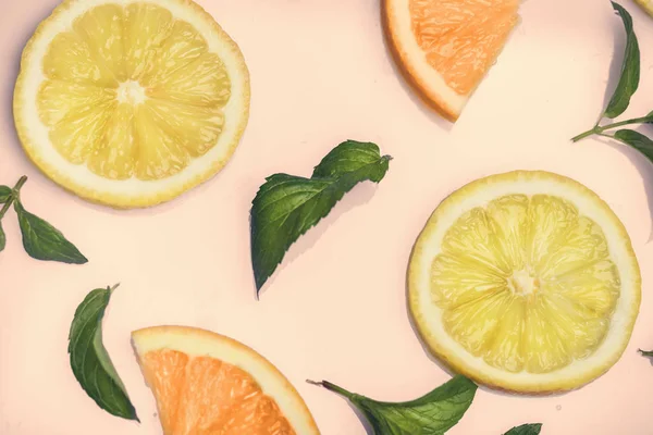 Citrus slices and mint herbs pattern on retro pink background from above. Top view of orange and lemon fruit slices on pastel background.