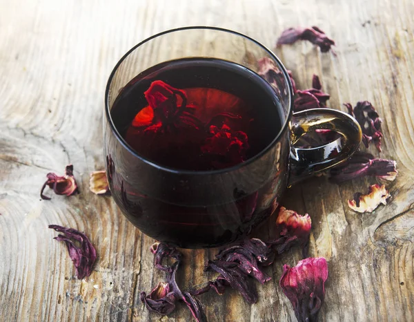 Hibiscus tea in teacup with dry hibiscus flower leaves. Organic herbal cup of tea on vintage wooden table background.