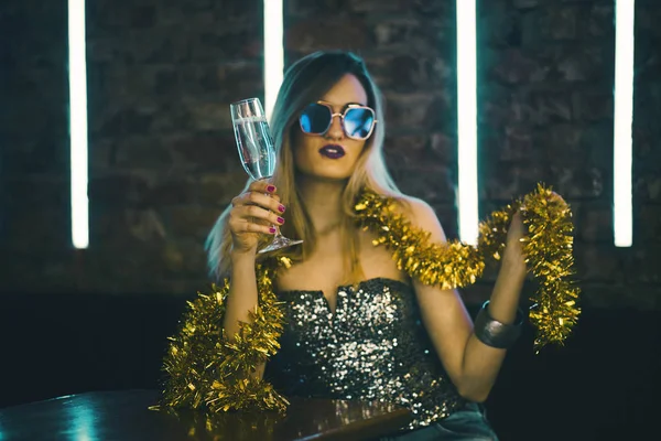 Young happy woman celebrating new year eve drinking champagne. Night lights and confetti. Lady clubber in nightclub having fun. Hipster girl at celebration luxury party.