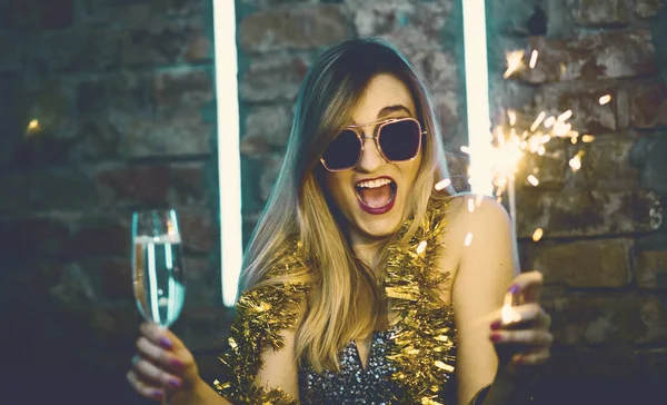 Young happy woman celebrating new year eve drinking champagne with fireworks. Lady clubber in nightclub having fun. Hipster girl at celebration luxury party.
