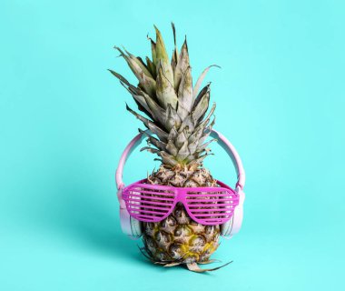 Güneş gözlüğü ve kulaklık ile moda trendy ananas meyve parlak pastel mavi arka plan üzerinde müzik dinleyin. Komik surat mavi ile serin hipster ananas. Yaz tatil tatil ve tropikal plaj partisi konsepti.