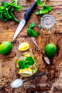 Mojito 'nun kaliteli ahşap masadaki malzemelerinin üst görüntüsü. Yukarıdan Küba kokteyli yapmak için nane, şeker ve limon dilimleri. Mutlu saat hazırlığı için dokulu arka planda taze capirinha içeceği.