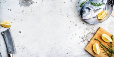 Tavada taze balık, limon ve biberiye kırsal beyaz mutfak masasında. Yukarıdan deniz yemeği hazırlığı. Lüks restoran menü tasarımı afiş çerçevesi. Arka planda deniz ürünleri var. Dorado tarif hazırlıyor.