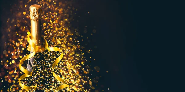 Luxury new year background. Champagne bottle with gold ribbon on dark background with golden bokeh glitter firework. Christmas celebration panoramic design banner.
