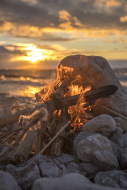 Gün batımında denize yakın bir ateş yakar.