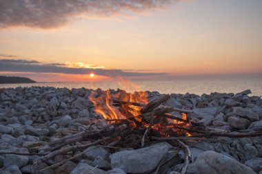 Gün batımında denize yakın bir ateş yakar.
