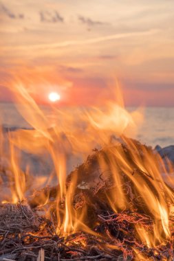 Gün batımında denize yakın bir ateş yakar.