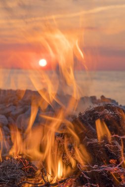 Gün batımında denize yakın bir ateş yakar.