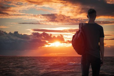 adam gün batımında deniz görünüyor.