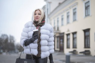 sarışın bir kürk manto kahve ile şehir etrafında yürür