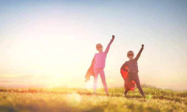 つの小さな子供たちは スーパー ヒーローを遊んでいます 夕焼け空の背景の子供たち 女の子パワー コンセプト — ストック写真