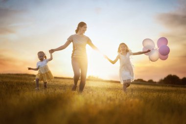 Mutlu sevgi dolu aile doğa üzerinde yaz aylarında eğleniyor. Genç anne ve iki kızı gülüyor ve çayır, gün batımı arka plan üzerinde oyun. 