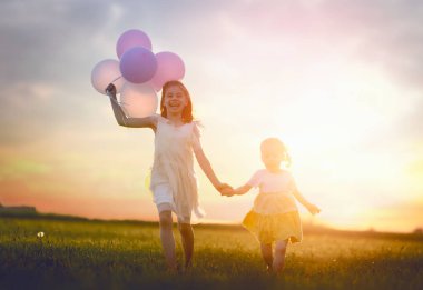 Mutlu çocuklar yaz aylarında doğa eğlenceli yaşıyorsanız. Çocuklar gülüyor ve çayır, gün batımı arka plan üzerinde oyun. Kız hava balonu ile çalışan.