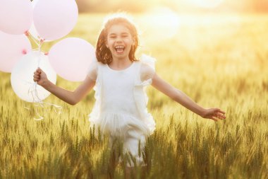 Mutlu bir çocukluk doğa üzerinde yaz aylarında eğleniyor. Çocuk gülüyor ve çayır, gün batımı arka plan üzerinde oyun. Kız hava balonu ile tahıl sahada çalışan.