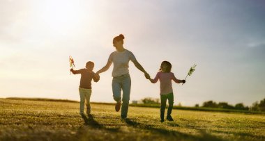 Mutlu sevgi dolu aile doğa üzerinde yaz aylarında eğleniyor. Genç anne ve iki kızı gülüyor ve çayır, gün batımı arka plan üzerinde oyun. 