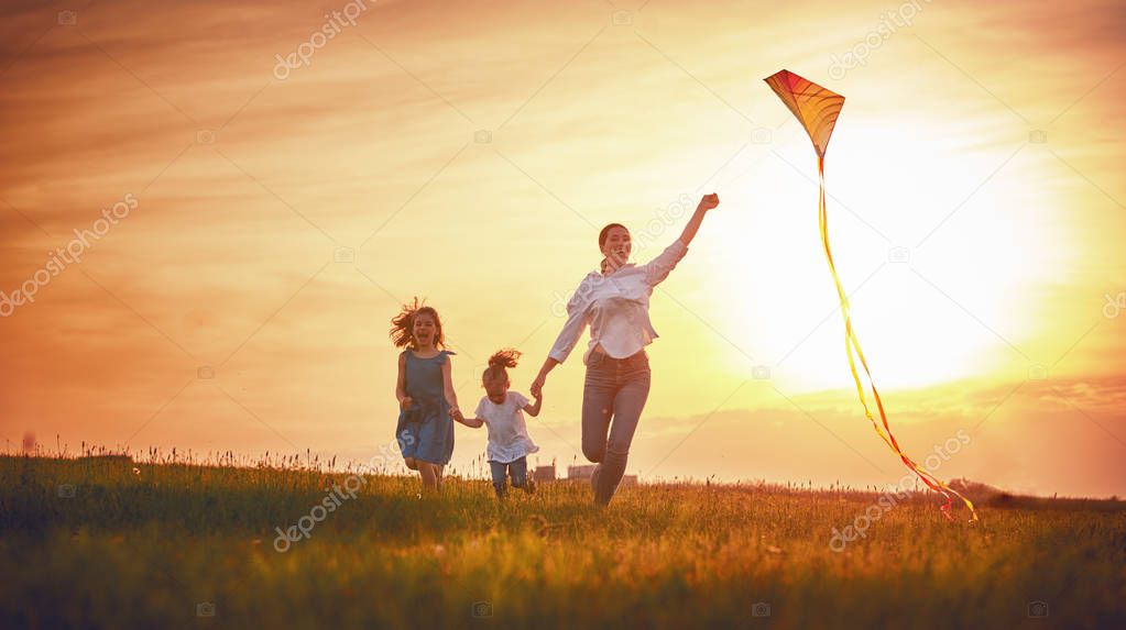 Happy family playing outdoor. Mother and children running on meadow with a kite in the summer on the nature.