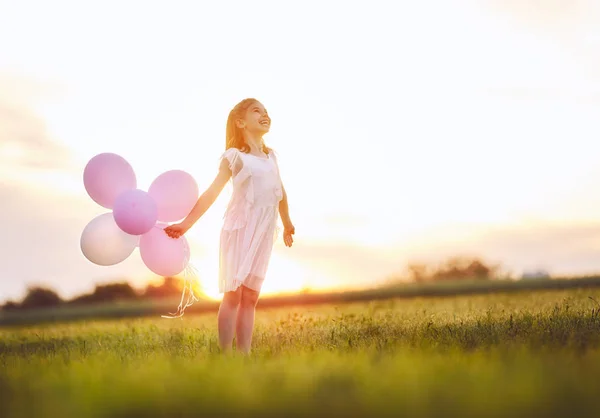 幸せな子供は夏に自然を楽しんでは 子は笑いと夕日を背景に牧草地に再生します 空気風船持つ少女 — ストック写真