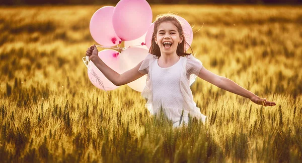 Mutlu bir çocukluk doğa üzerinde yaz aylarında eğleniyor. Çocuk gülüyor ve çayır, gün batımı arka plan üzerinde oyun. Kız hava balonu ile tahıl sahada çalışan.