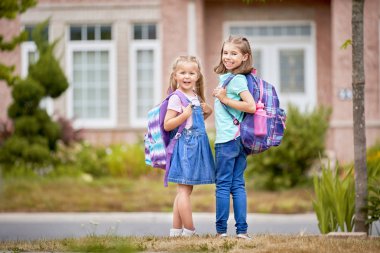İlköğretim Okulu öğrencileri. Açık havada bina yakınındaki sırt çantaları kızlarla. Ders başlangıcı. Sonbaharın ilk günü.