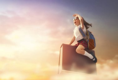 Okula dönün! Mutlu şirin, çalışkan çocuk günbatımı gökyüzünün arka planında kitabın üzerinde uçuyor. Eğitim ve okuma kavramı. Hayal gücünün gelişimi..