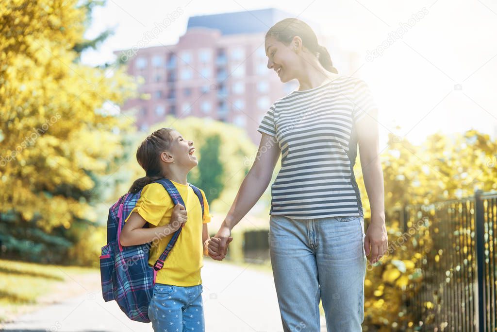 Parent and pupil of primary school go hand in hand. Woman and girl with backpack behind the back. Beginning of lessons. First day of fall.