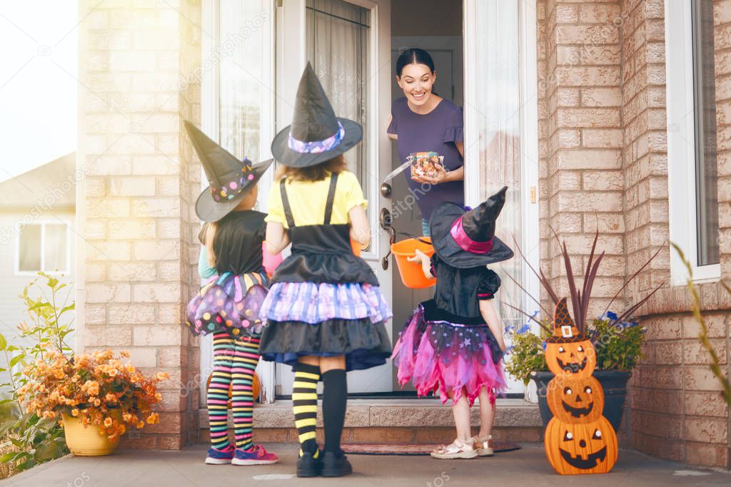 Happy family celebrating Halloween! Young mom treats children with candy. Funny kids in carnival costumes.