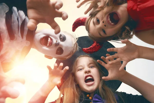 Happy brother and two sisters at Halloween. Funny kids in carnival costumes outdoors. Cheerful children on sunset background.