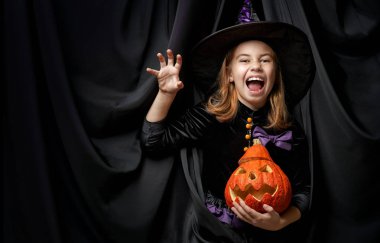 Cadılar Bayramınız Kutlu Olsun! Sevimli küçük gülen kız cadı kostüm siyah duvar arka plan üzerinde. 