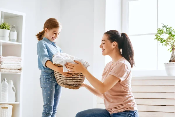 美しい若い女性と子供の女の子の小さなヘルパーは家で洗濯をしながら楽しさと笑顔を持っています — ストック写真