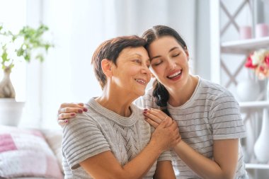 Güzel anne ve kız evdeki kanepede otururken sarılıyor, konuşuyor ve gülümsüyor..