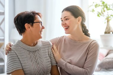 Güzel anne ve kız evdeki kanepede otururken sarılıyor, konuşuyor ve gülümsüyor..