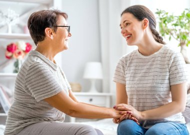 Güzel anne ve kız evdeki kanepede otururken sarılıyor, konuşuyor ve gülümsüyor..