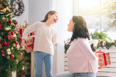 Mutlu Noeller ve mutlu tatiller! Neşeli anne ve tatlı kızı hediye değiş tokuşu yapıyor. Ebeveyn ve küçük çocuk kapalı alanda eğleniyorlar. Odasında hediyeler olan sevgi dolu bir aile.